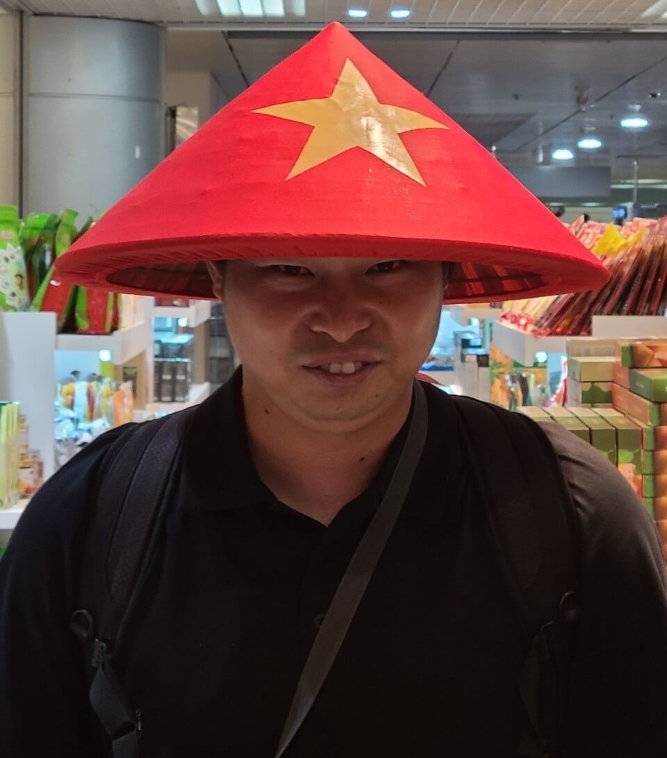 竹山がホーチミンの空港で現地の帽子「ノンラー」を被って記念撮影する様子
